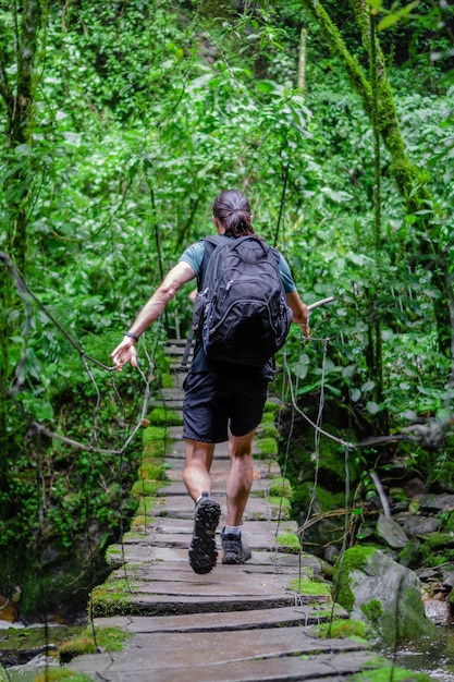 Jovem latino na selva atravessando uma ponte suspensa de madeira caminhada ecológica foto vertical