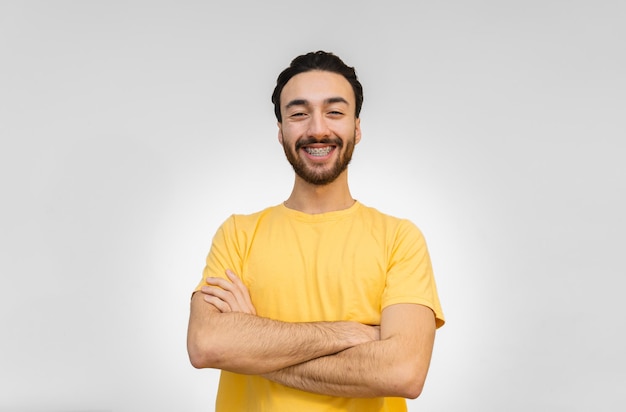 Jovem latino olhando para a câmera rindo com os braços cruzados postura confiante fundo branco