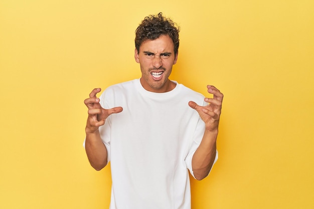 Foto jovem latino posando em fundo amarelo chateado gritando com mãos tensas