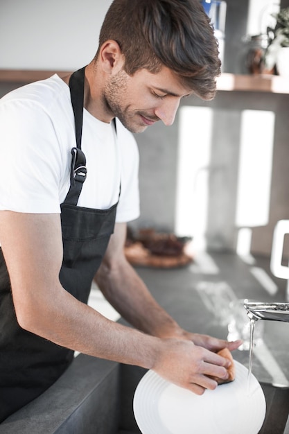 Jovem lava pratos em sua cozinha