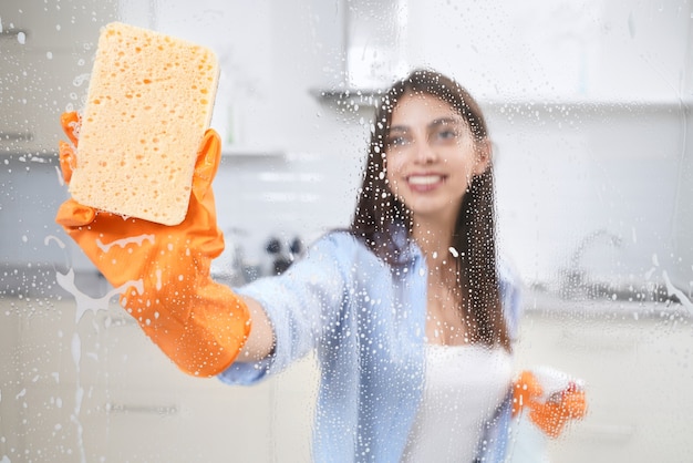 Jovem lavando janela com pano e detergente