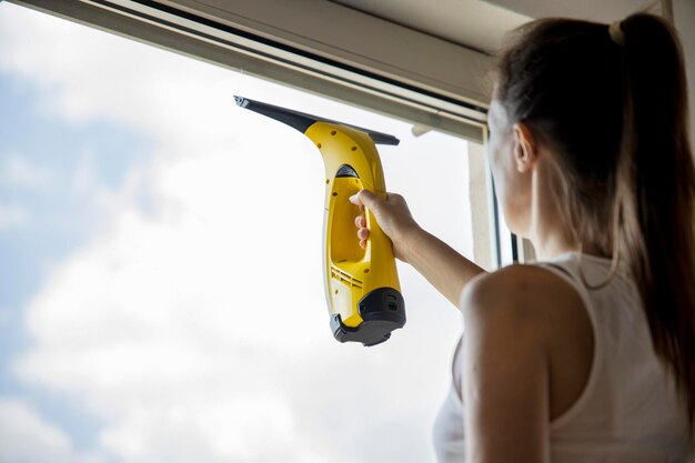 Foto jovem lavando janelas com limpador de janelas dentro de casa