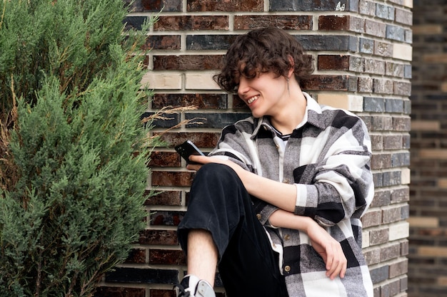 jovem lê algo no telefone enquanto está sentado na calçada de tijolos