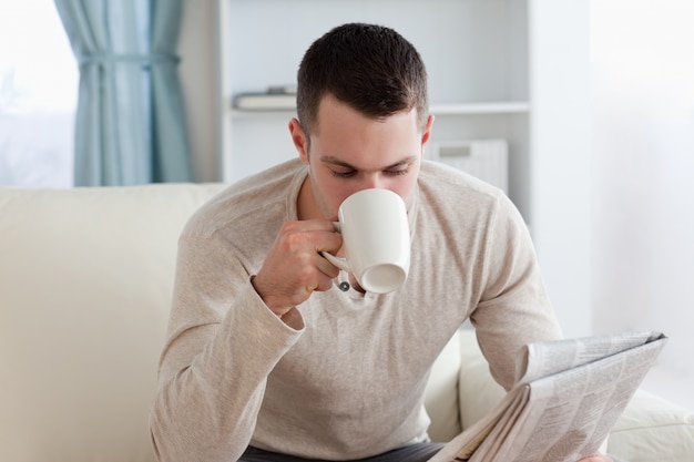 Jovem lê as notícias enquanto toma um café