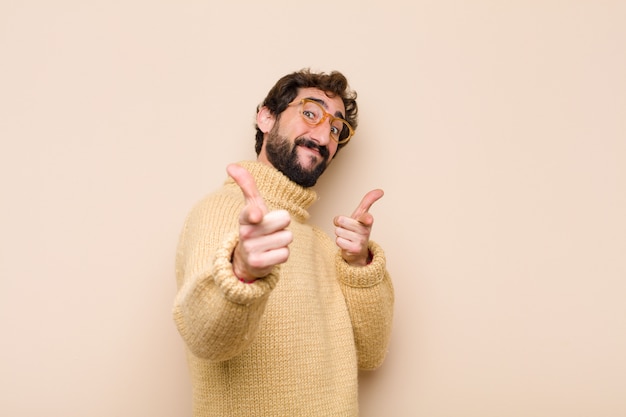 Jovem legal, sentindo-se feliz, legal, satisfeito, relaxado e bem-sucedido, apontando a câmera, escolhendo-o contra a parede plana