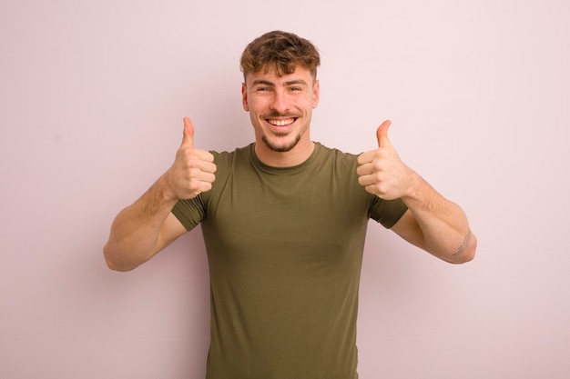 Jovem legal sorrindo amplamente olhando feliz positivo confiante e bem sucedido com os dois polegares para cima