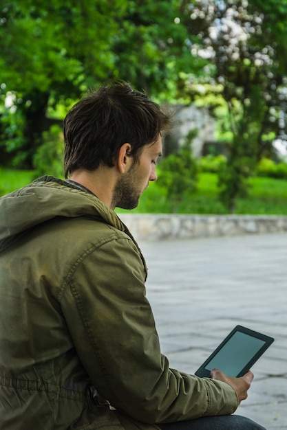 Jovem lendo tablet digital no parque