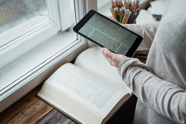 Jovem lendo tablet pc e livros na frente da grande janela