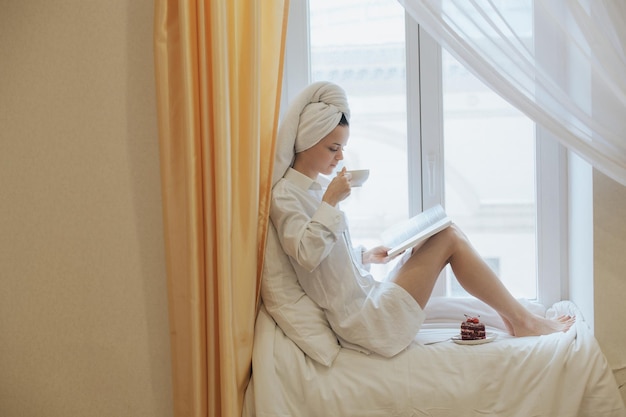 Jovem lendo um livro ao lado da janela depois de se levantar de manhã Conceito de estilo de vida matinal