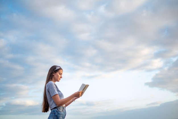 Jovem lendo um livro com céu azul