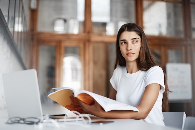 Jovem lendo um livro e usando um notebook para obter conhecimentos em um café luminoso. conceito de educação.