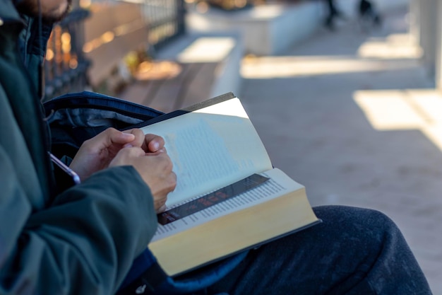 Jovem lendo um livro sentado em um banco em um parque