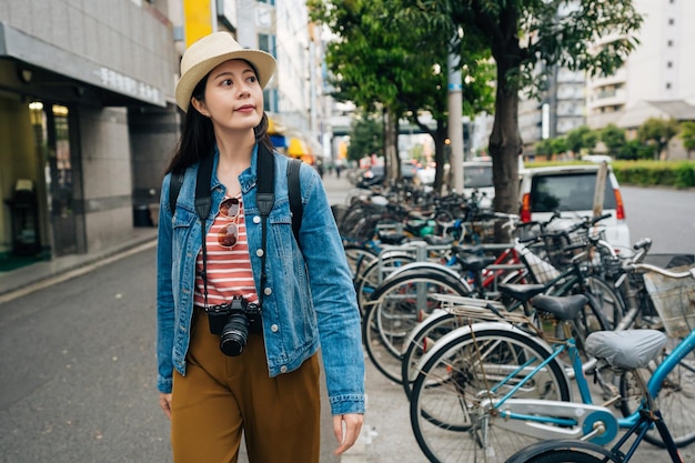 jovem lente viajar andando na estrada em osaka japão. muitos parque de bicicletas do lado da rua na zona urbana tranquila. mulher carregando câmera visitando auto viagem em jp.