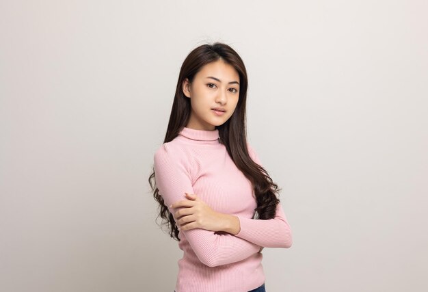 Jovem linda adolescente asiática de camisa rosa em pé e sorria em fundo branco isolado