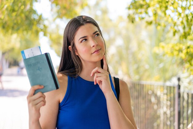 Jovem linda brasileira ao ar livre, segurando um passaporte e pensando