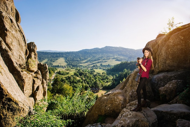 Jovem linda com câmera fotográfica vintage nas montanhas rochosas com paisagem cênica ao fundo