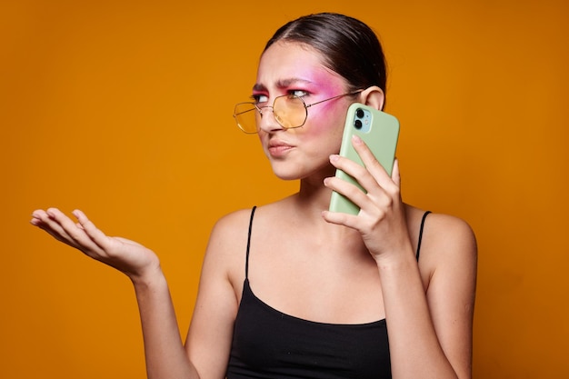 Foto jovem linda com um telefone na mão maquiagem brilhante posando emoções de moda fundo amarelo inalterado