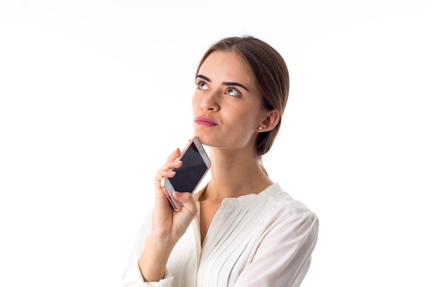 Jovem linda de blusa branca segurando seu celular rosa em fundo branco no estúdio