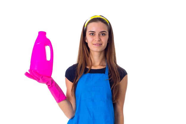 Jovem linda de camiseta azul e avental com luvas cor de rosa segurando detergente no estúdio