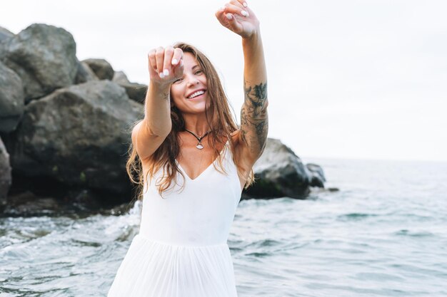 Jovem linda e despreocupada com cabelo comprido em vestido branco curtindo a vida na praia do mar