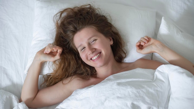 Jovem linda e feliz com sono na cama no quarto em casa pela manhã, deitada sob o branco