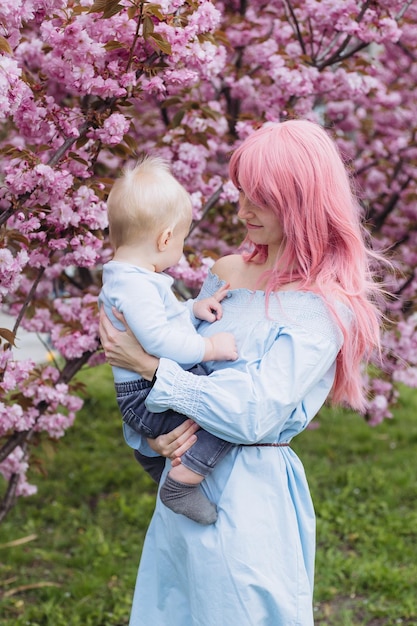 Jovem linda e filho pequeno na natureza brincando no parque primavera nos jardins floridos de sakura garotinho e mãe se divertem na atividade de fim de semana