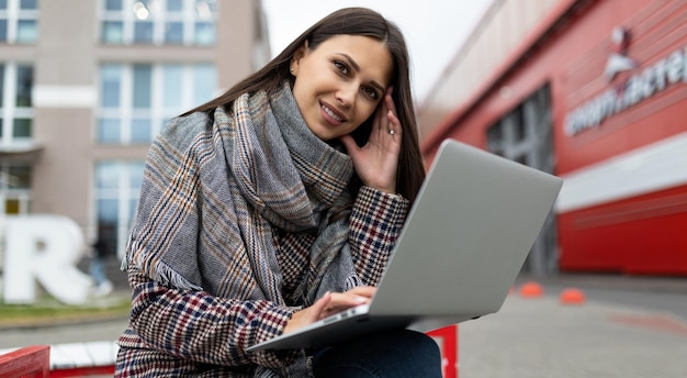 Jovem linda em um casaco de outono com um laptop no fundo dos edifícios da cidade