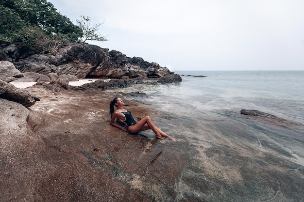 Jovem linda em um maiô preto fechado relaxa e toma sol na praia na tailândia em phuket