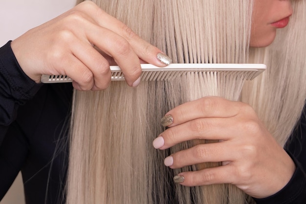 Jovem linda escovando seu cabelo loiro longo e saudável no salão de cabeleireiro