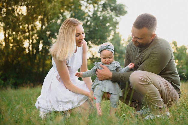 Jovem linda família com uma filha abraça, beija e anda na natureza ao pôr do sol. Foto de uma família com uma criança pequena na natureza.