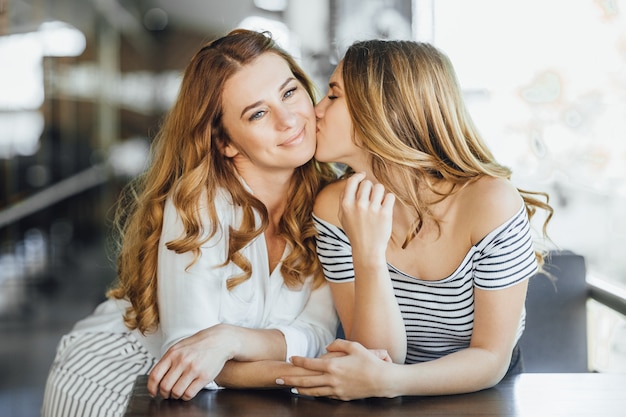 Jovem linda filha adolescente beijando a mãe em um café com esplanada de verão em roupas casuais.