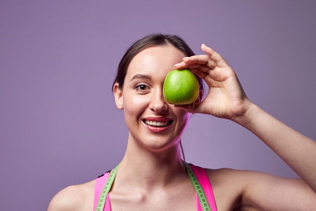 Jovem linda garota esportes em leggings e um top com uma fita métrica em volta do pescoço, segurando uma maçã verde. Estilo de vida saudável.