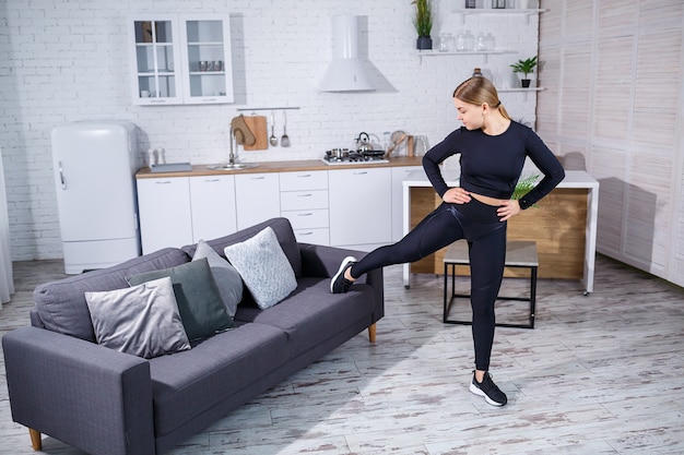 Jovem linda garota esportes em uma legging e um top faz exercícios em casa no sofá. estilo de vida saudável. a mulher pratica esportes em casa.