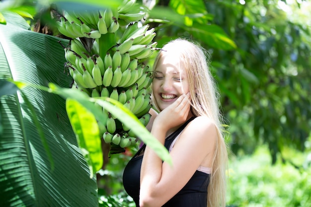 Jovem linda garota loira parada perto de uma bananeira
