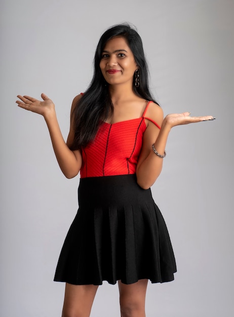 Jovem linda garota sorridente com roupa vermelha e preta, posando em fundo cinza.