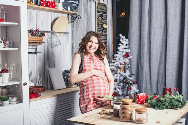 Jovem linda grávida em casa na cozinha sorrindo feliz