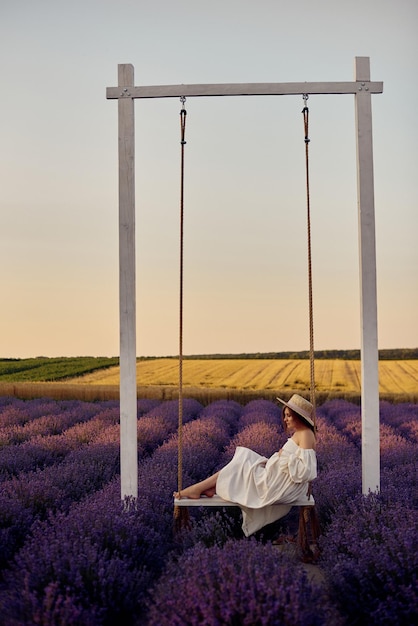 Jovem linda grávida em um balanço em um campo de lavanda ao pôr do sol