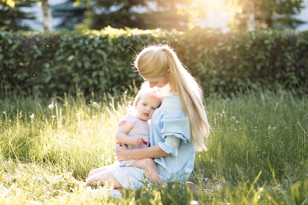 Jovem linda loira mãe com sua filha rindo juntas e brincando no parque verde