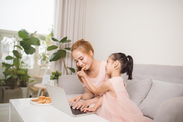 Jovem linda mãe asiática ensinando filha usando computador sentado no sofá em casa