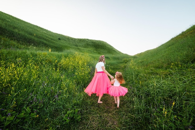 Foto jovem linda mãe com a filha com a mesma roupa família com o mesmo visual estilo de moda roupas para pais e filhos férias em família nas montanhas mãe e menina caminhando ao ar livre vista traseira