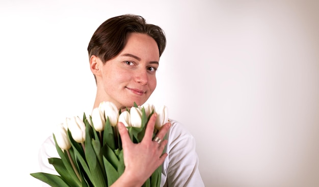 Jovem linda modelo bonito com tulipas em um fundo branco, sorrindo e olhando para a vista frontal da câmera Menina com olhos castanhos, segurando um buquê de flores