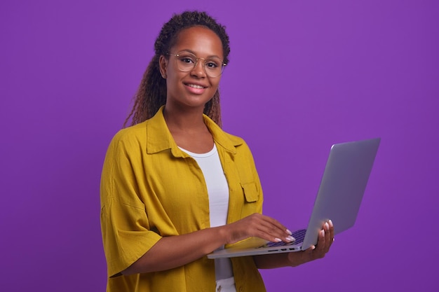 Jovem linda mulher afro-americana sorridente com laptop aberto fica no estúdio