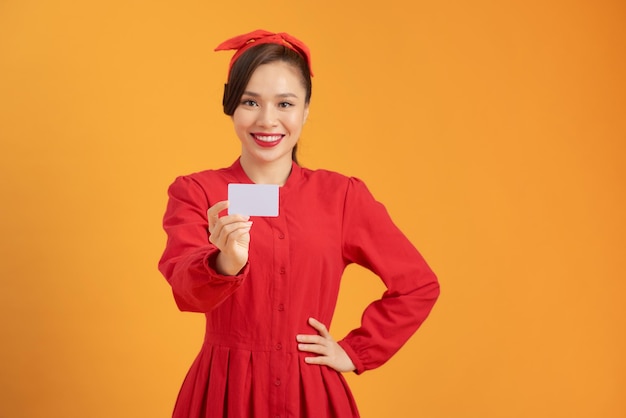 Jovem linda mulher asiática segurando cartão de crédito sobre fundo laranja isolado