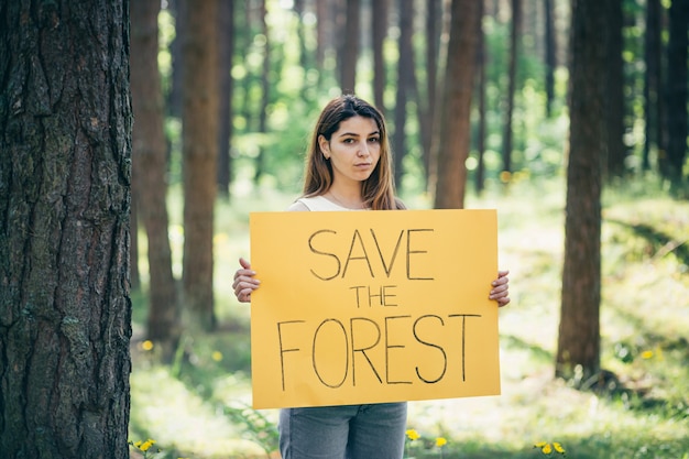 Jovem, linda mulher, ativista voluntária na floresta com um pôster salve a floresta