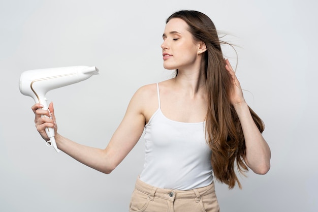 Jovem linda mulher confiante usando secador de cabelo isolado no fundo branco