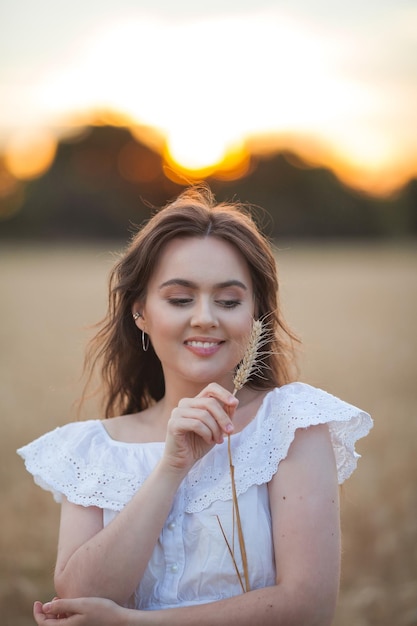 Jovem linda mulher de 1920 anos com cabelos escuros em um vestido branco estilo boho em um campo de trigo ao pôr do sol Retrato de modelo jovem feliz de verão