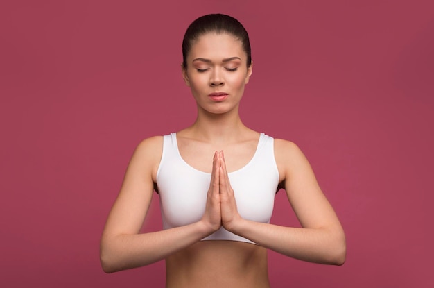 Jovem linda mulher de cabelos castanhos caucasiana praticando meditação de ioga com os olhos fechados fazendo namaste mudra isolado em fundo rosa