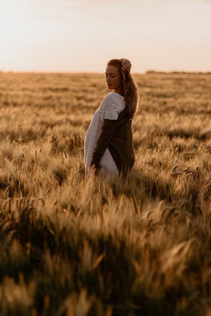 Jovem linda mulher grávida vestida de branco, andando no campo de trigo laranja em um dia ensolarado de verão. natureza no país. expectativa de milagre. pôr do sol no isolamento.