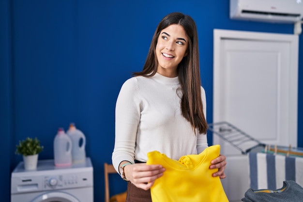 Jovem linda mulher hispânica sorrindo confiante dobrando roupas na lavanderia