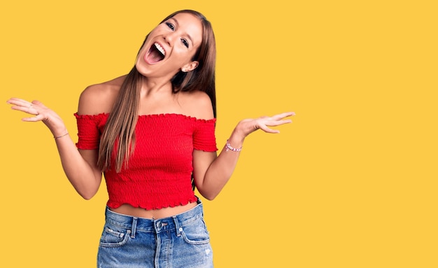 Foto jovem linda mulher hispânica vestindo roupas casuais comemorando loucamente e maravilhada pelo sucesso com os braços levantados e olhos abertos gritando o conceito de vencedor animado